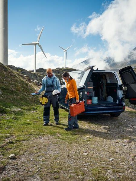 ID. Buzz Cargo im Gebirge, zwei Handwerker gehen auf Windräder zu