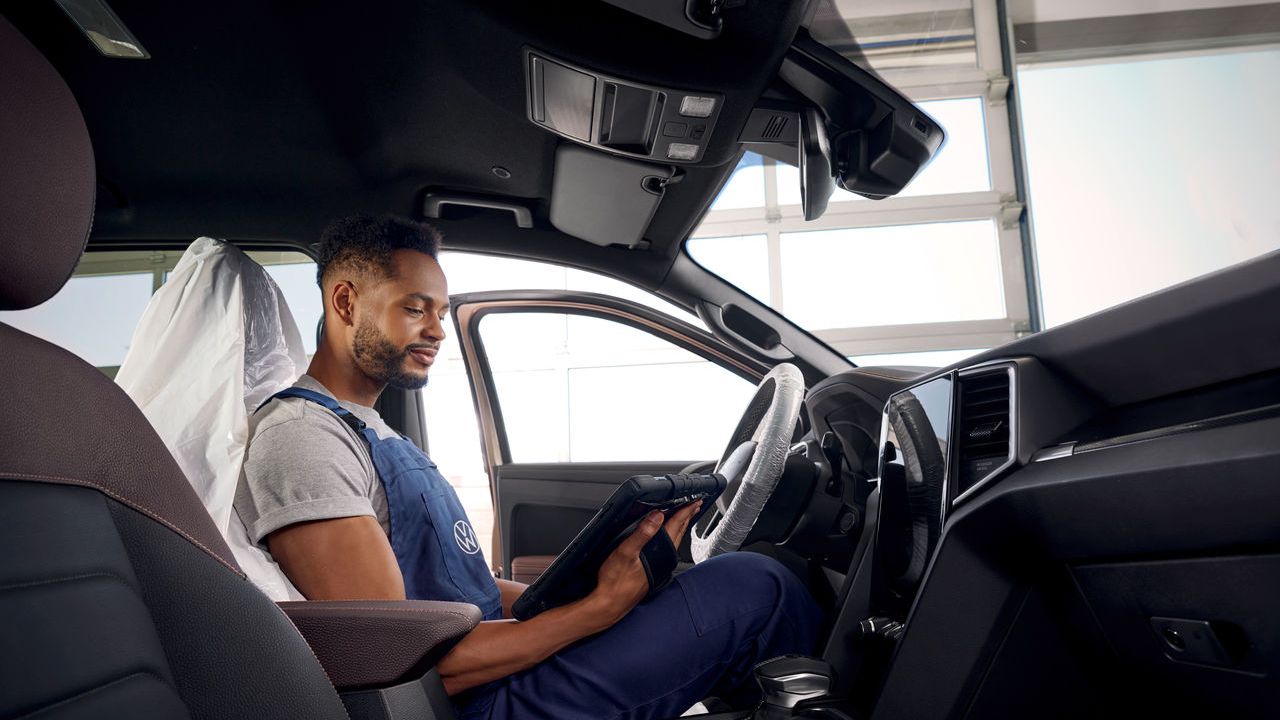 Ein Volkswagen Mechaniker sitzt in einem Volkswagen Nutzfahrzeug und blickt auf sein Tablet.