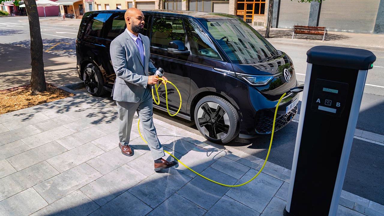 Ein Mann im Anzug lädt seinen schwarzen Volkswagen ID. Buzz an einer Ladesäule.
