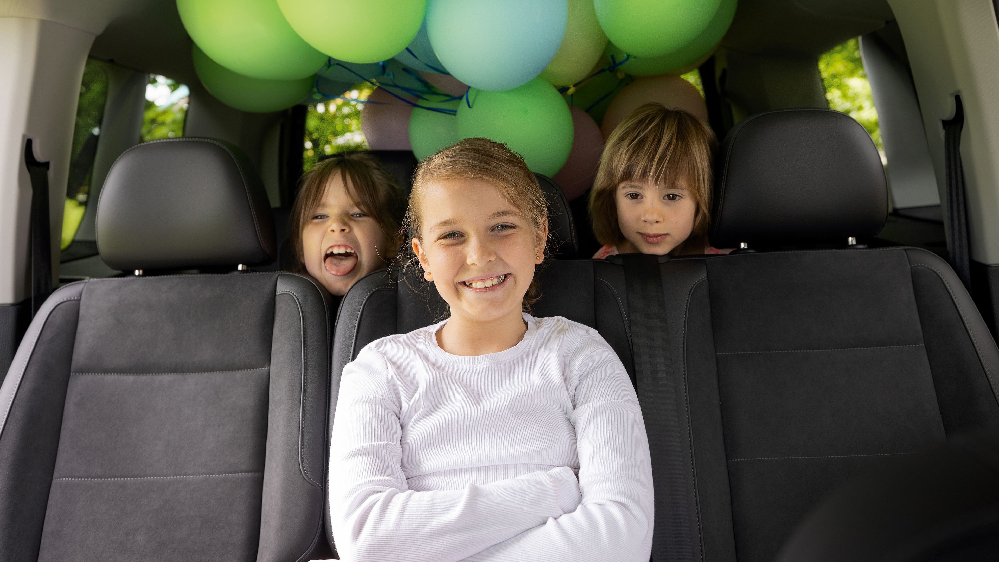 Kinder sitzen mit Luftballons im VW Caddy und haben Spaß