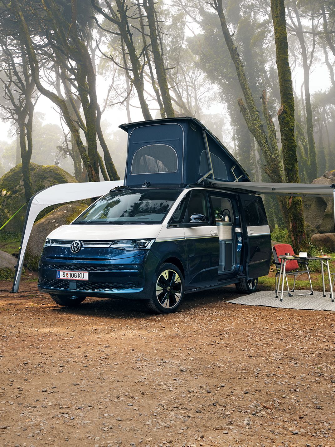New California steht mit ausgeklapptem Dach und ausgefahrener Marquise in einem Wald, Campingstühle stehen unter der Marquise