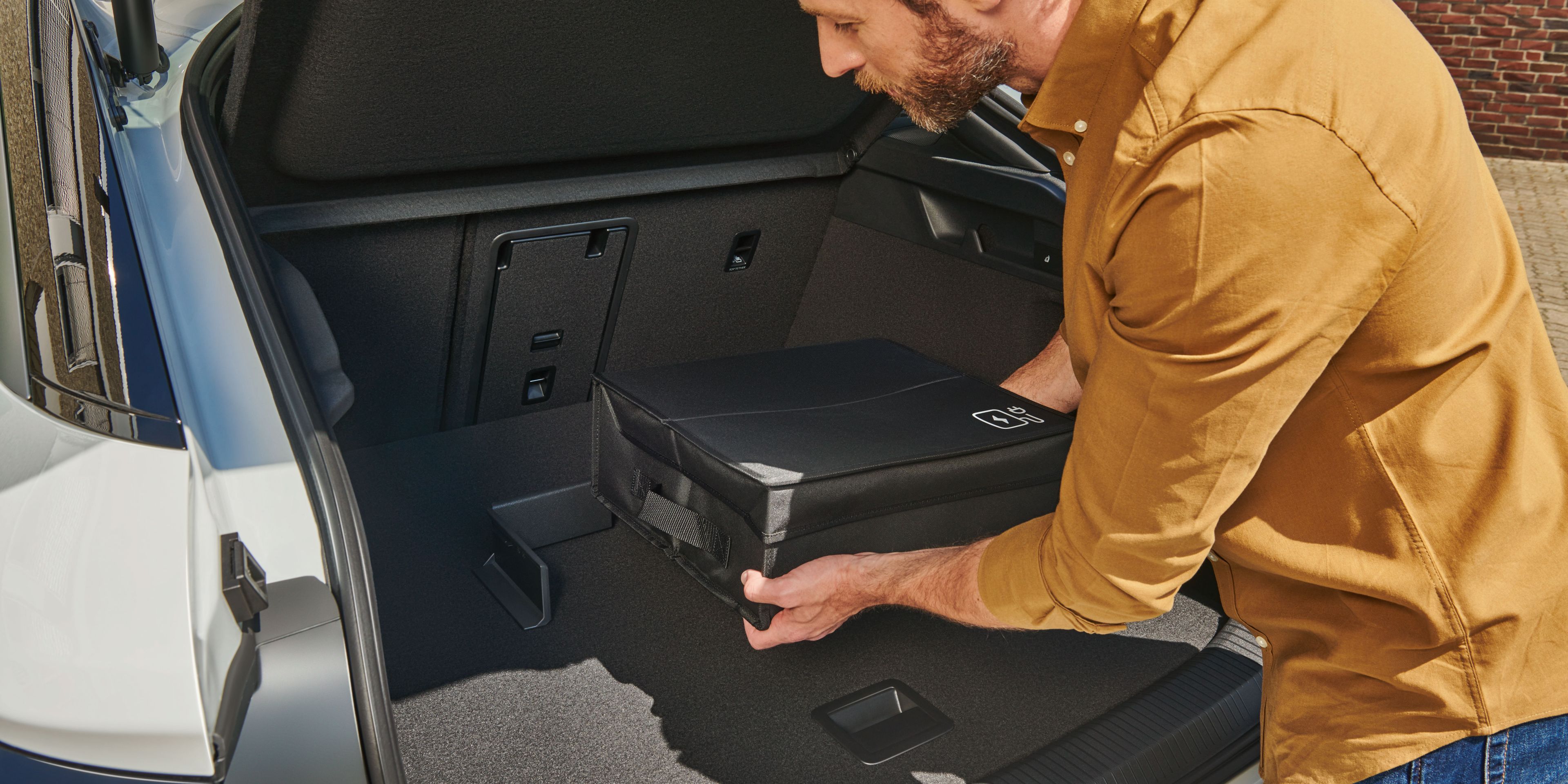 Ein Mann befestigt eine Tasche mit Volkswagen Original Cargo Elementen im Kofferraum eines Volkswagen ID.7.