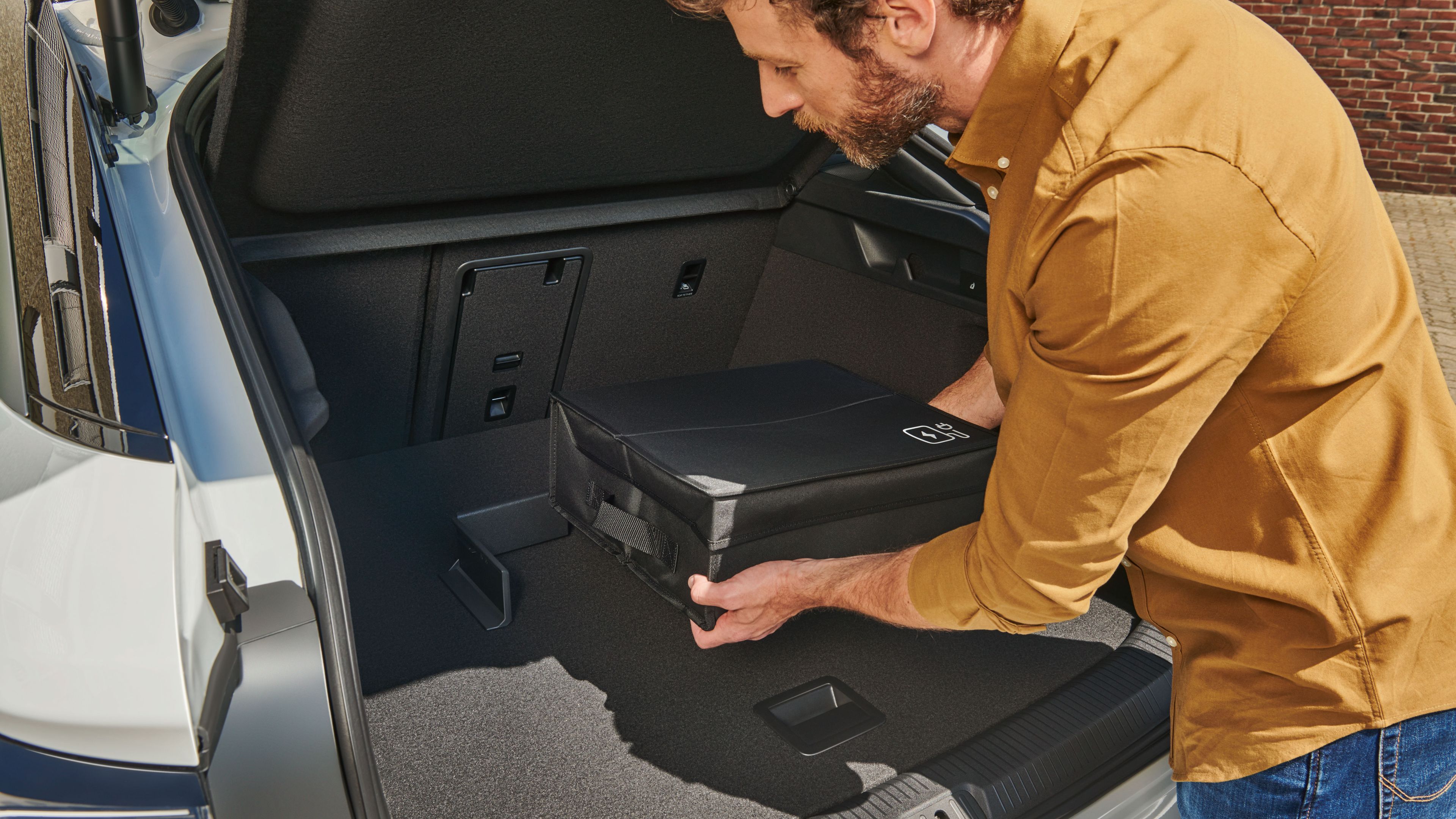 Ein Mann befestigt eine Tasche mit Volkswagen Original Cargo Elementen im Kofferraum eines Volkswagen ID.7.