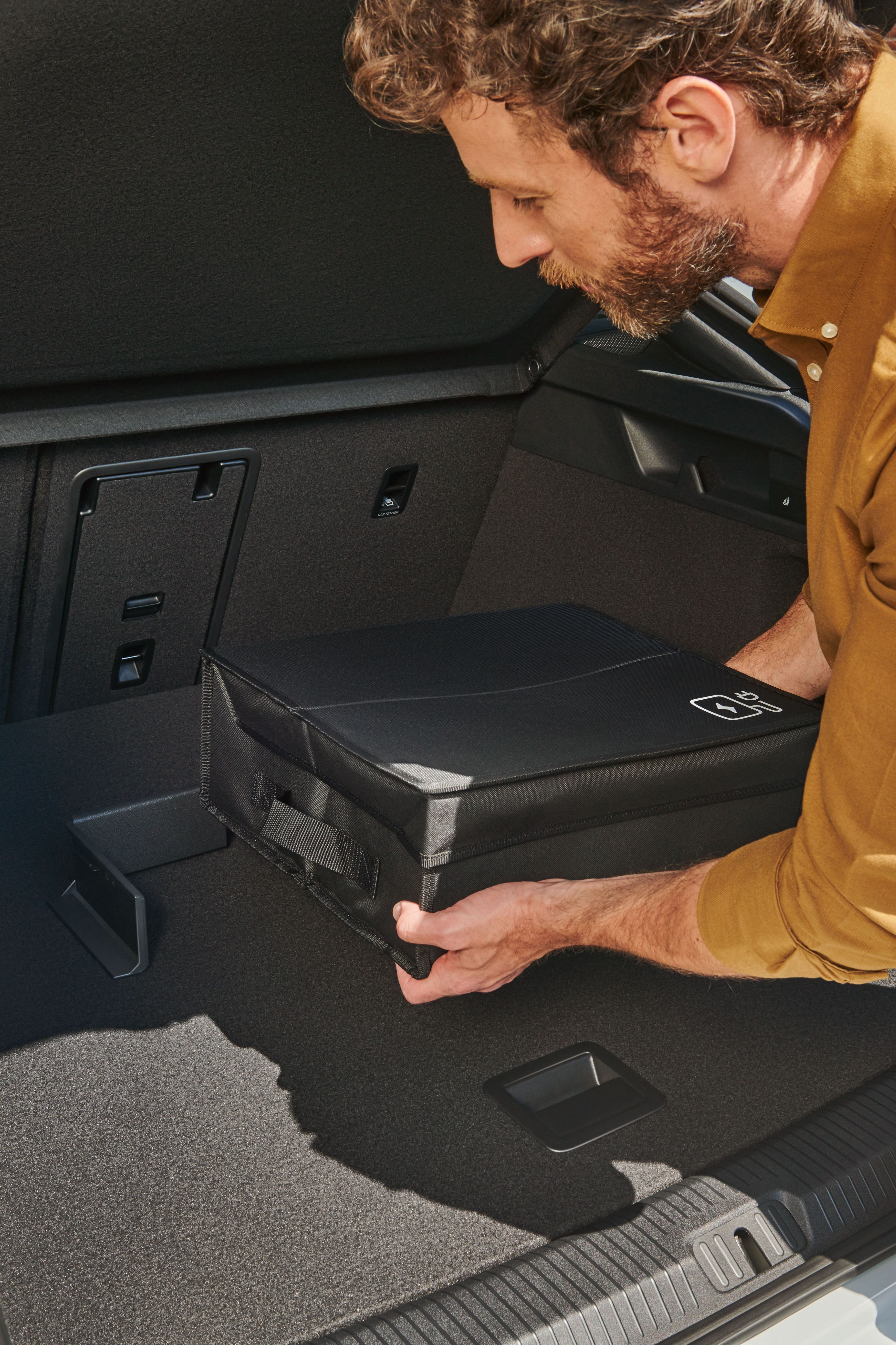 Ein Mann befestigt eine Tasche mit Volkswagen Original Cargo Elementen im Kofferraum eines Volkswagen ID.7.