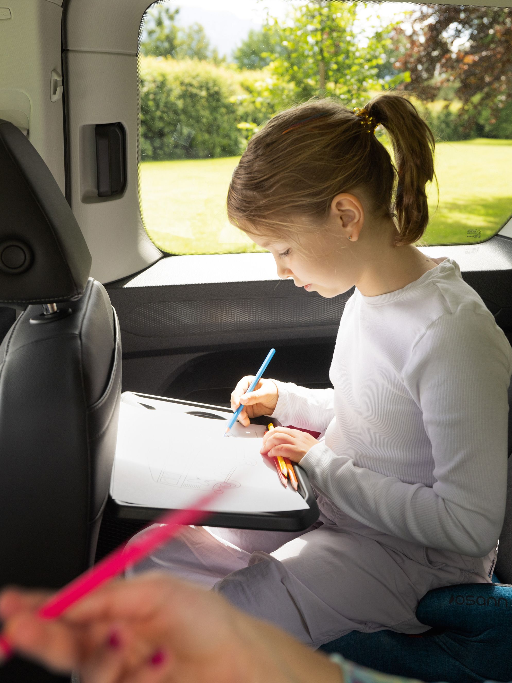 Kinder zeichnen im VW Caddy auf ausklappbaren Tischen der Rückseite der Vordersitze
