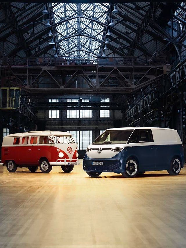 Ein roter VW Bulli und ein blauer Volkswagen ID. Buzz Cargo in schräger Seitenansicht in einer Werkshalle.