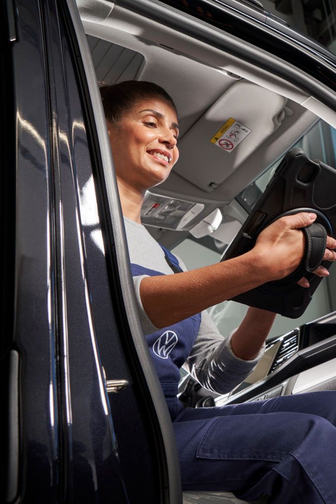 Eine Volkswagen Service Technikerin sitzt in einem Volkswagen Nutzfahrzeug und blickt auf ein Tablet.