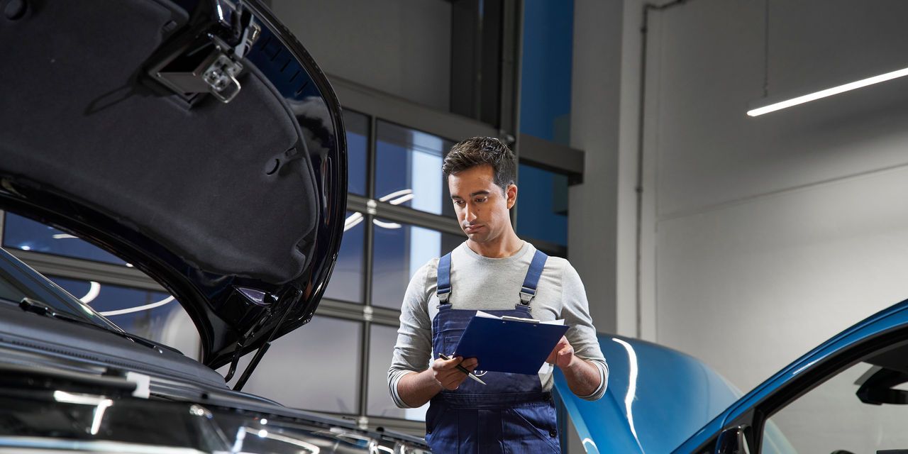 überprüft einen roten und einen blauen Volkswagen in einer Werkstatt. Die Volkswagen Werkstatt hat moderne Beleuchtung und große Fenster im Hintergrund.
