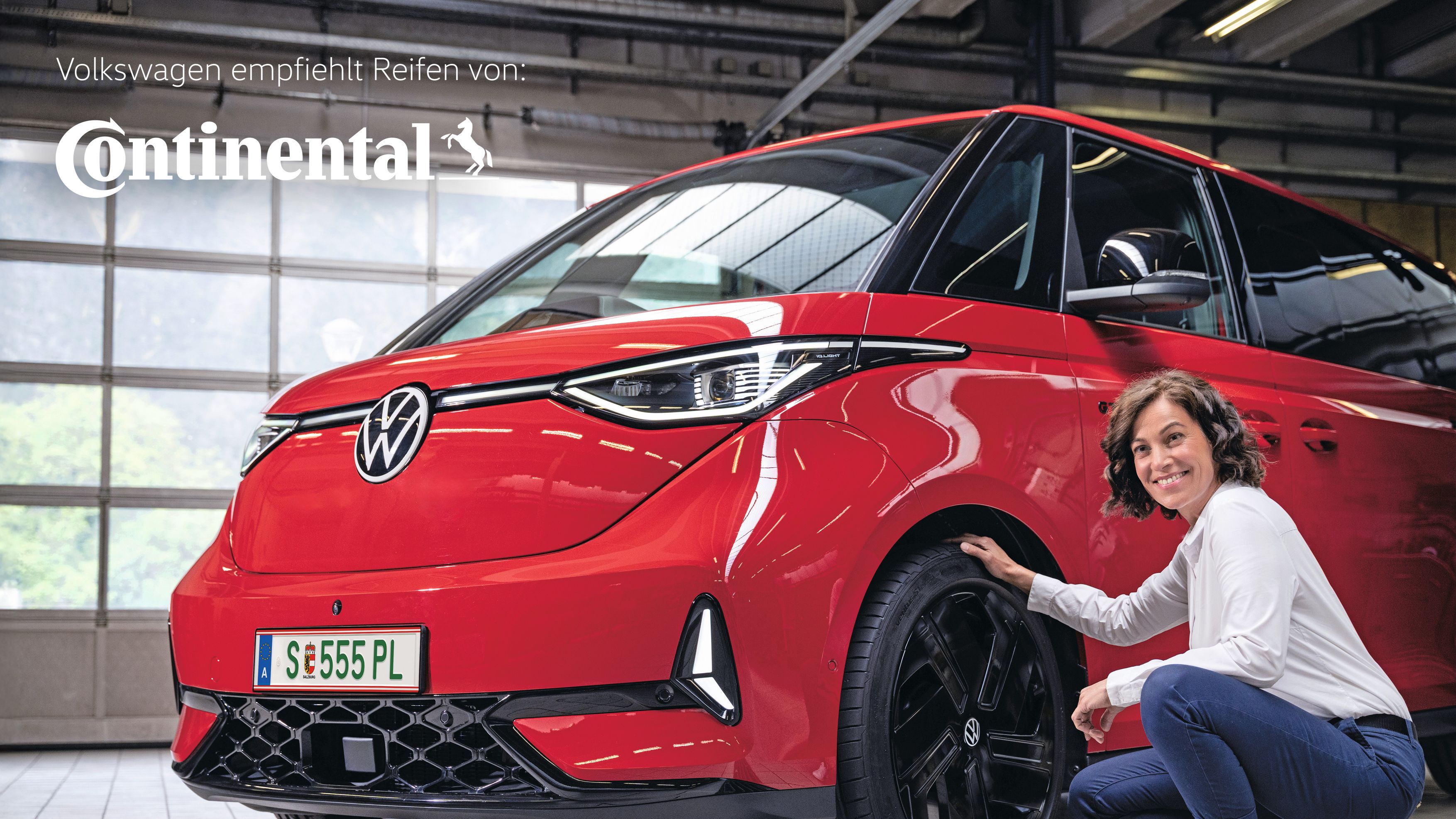 Ein Frau lächelnd in der Hocke vor einem roten Volkswagen ID. Buzz.