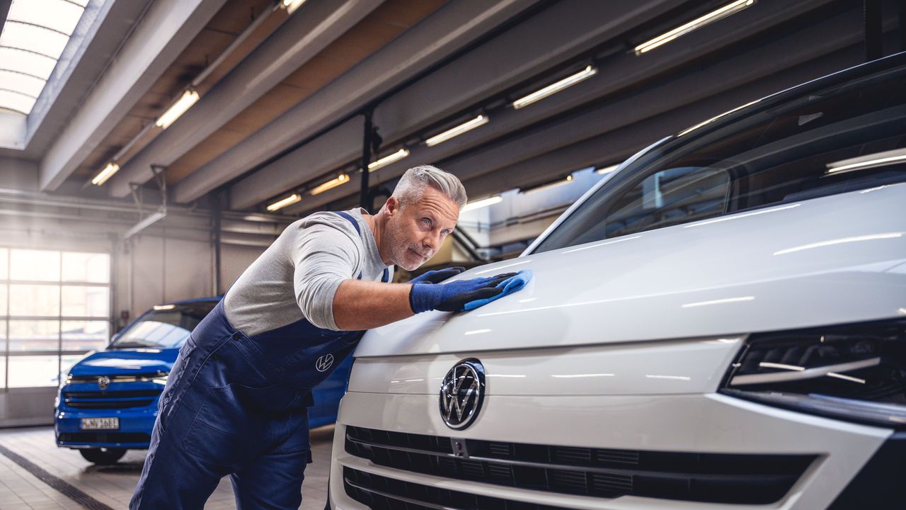 Ein Volkswagentechniker poliert den Lack eines Volkswagen Nutzfahrzeugs mit einem Tuch.