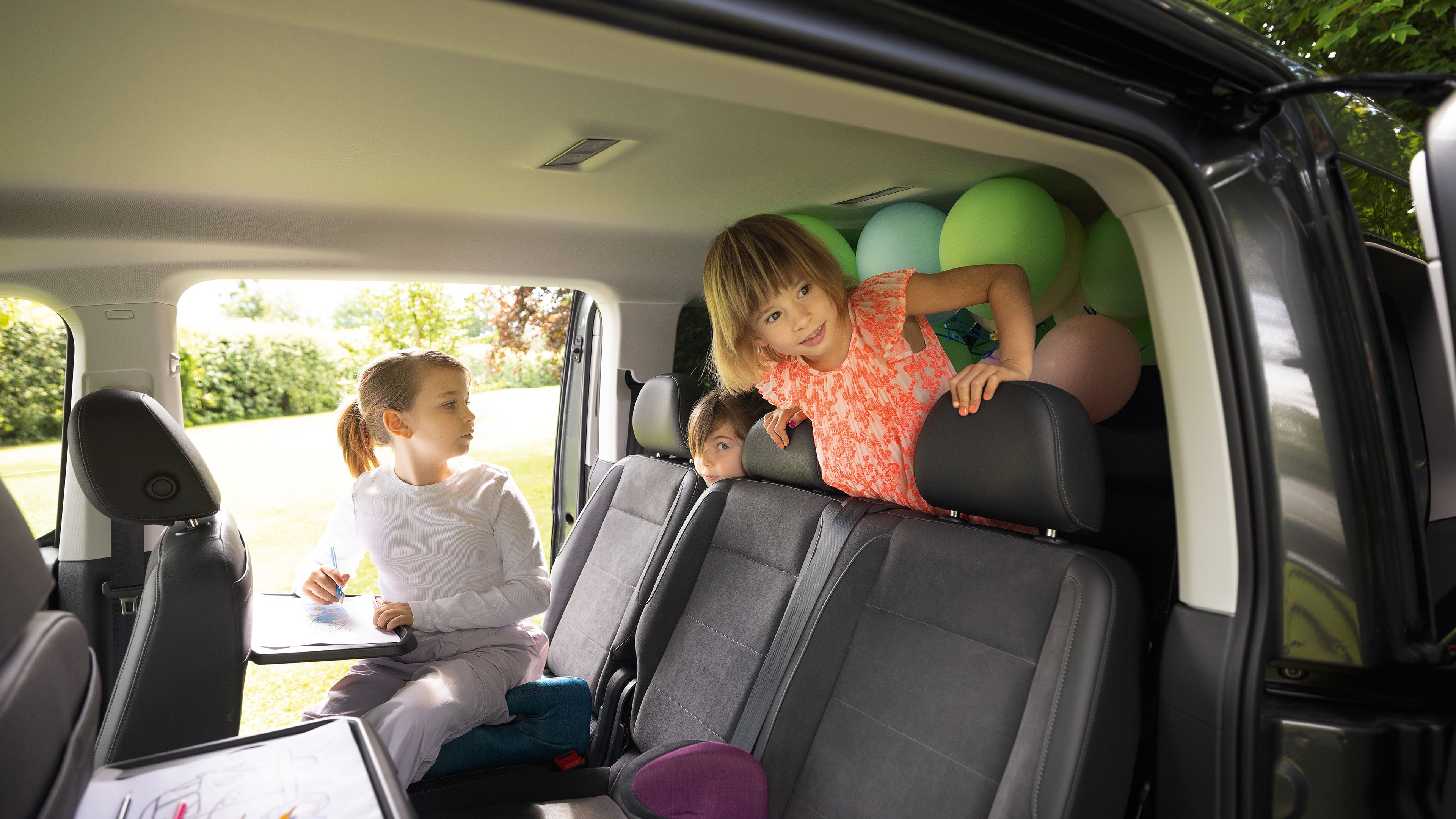 Kinder sitzen im parkenden VW Caddy und malen auf ausklappbaren Tischen der Vordersitze