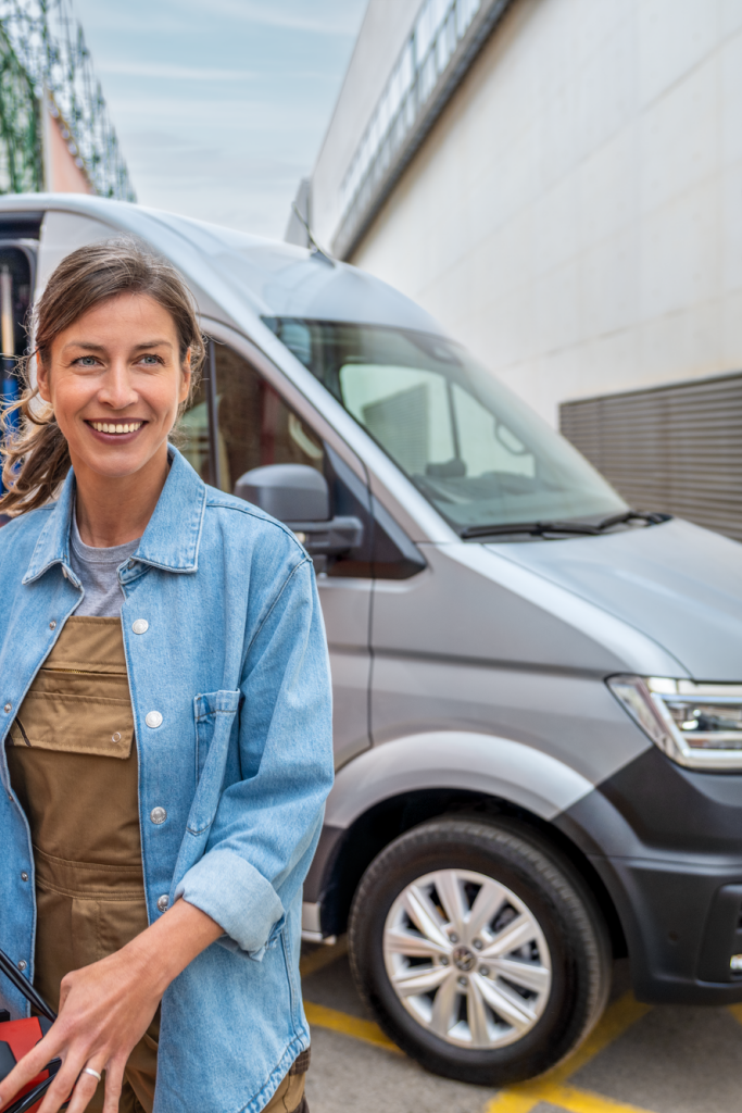 Eine Frau vor einem silbernen Crafter Kastenwagen, ein Mann kniet auf der Ladefläche.
