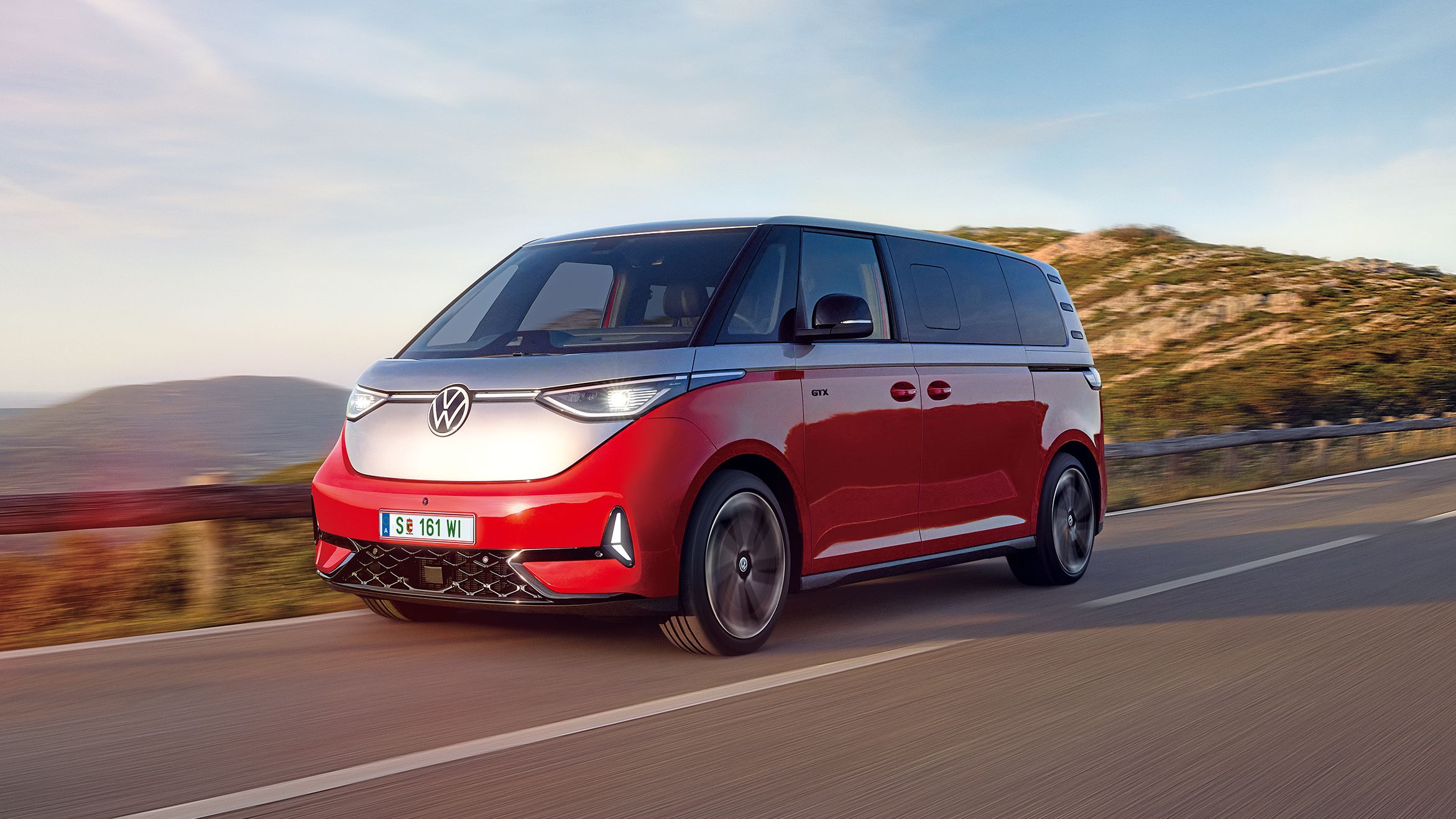 Ein rot - silberner ID. Buzz fährt entlang einer Straße in den Bergen