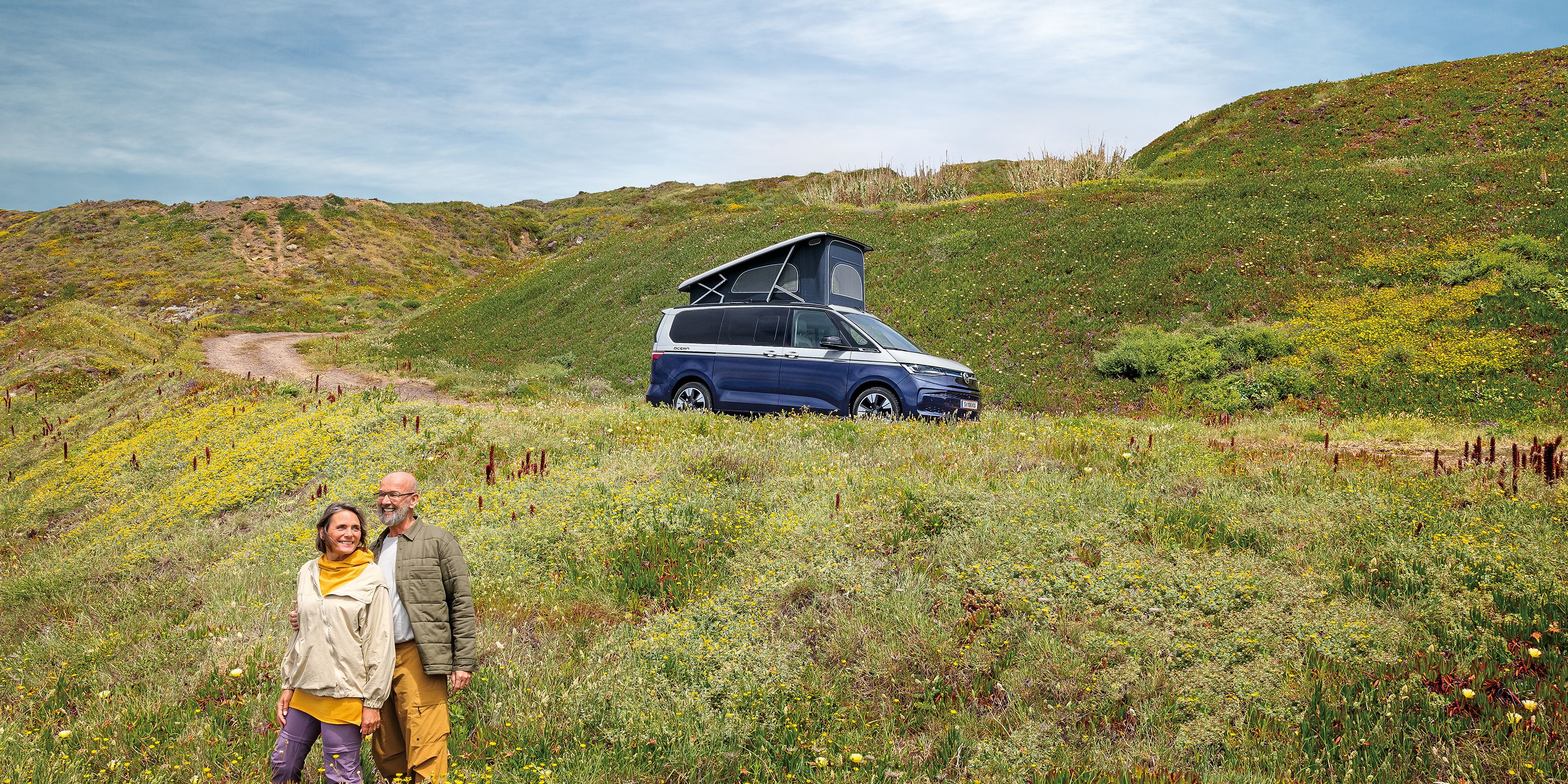 Ein VW California steht auf einer Schotterstraße am Meer