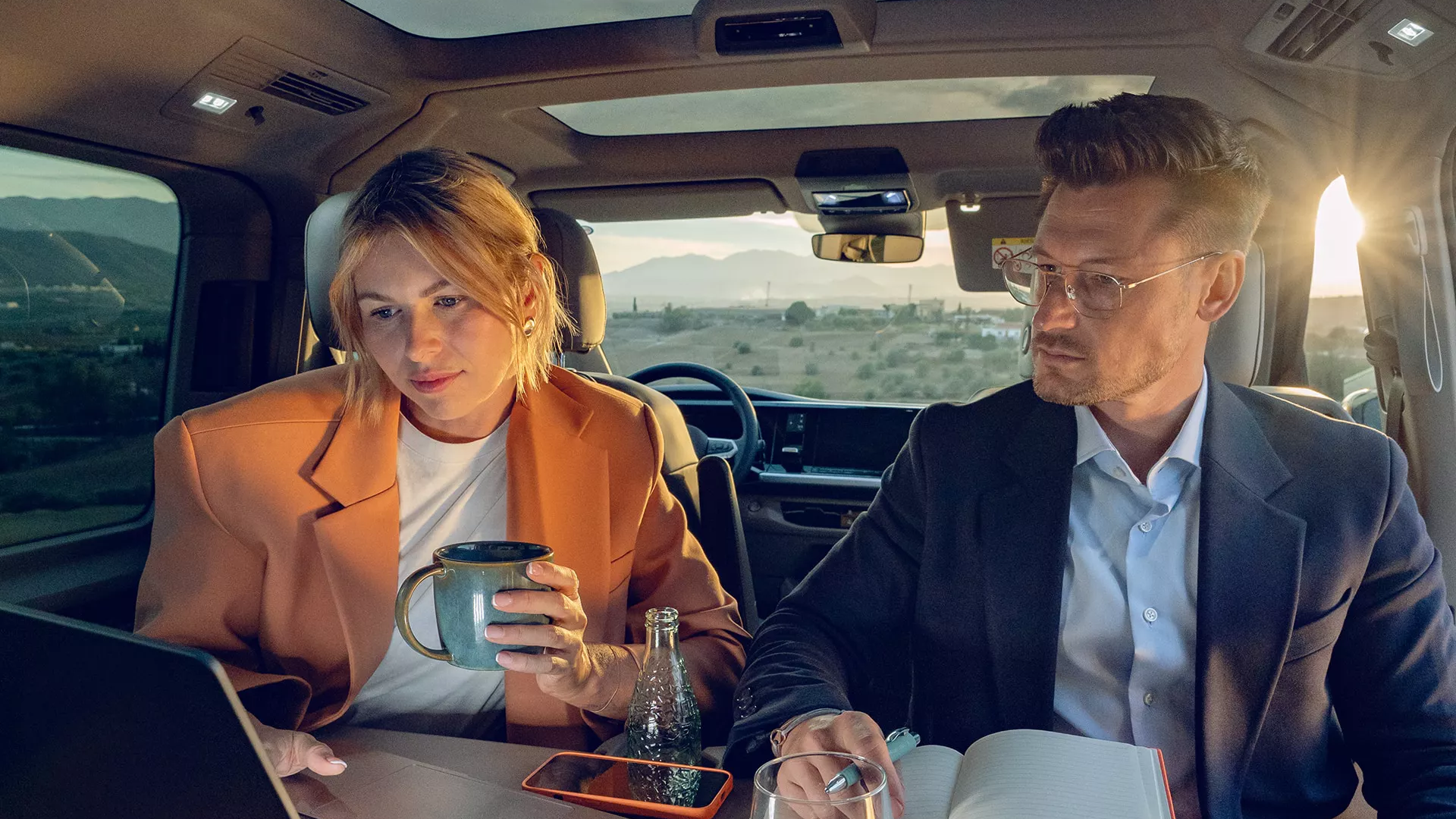Mann und Frau sitzen im Fond eines neuen VW Multivans, ausgeklappter Tisch, schauen auf Laptop