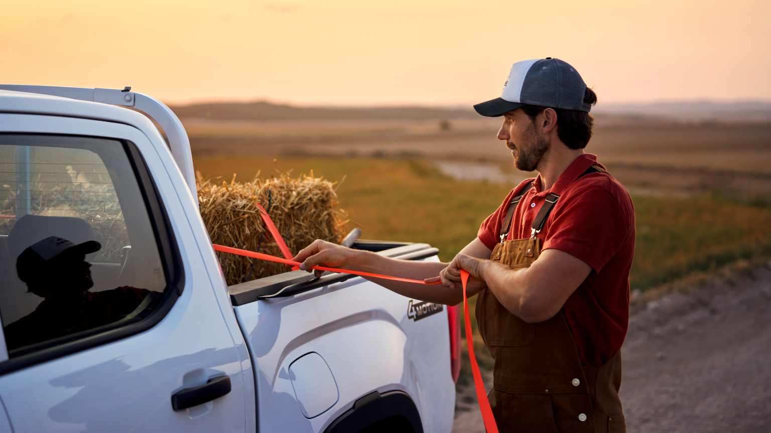 Ein Mann zurrt einen Strohballen an der Ladefläche eines Volkswagen Amarok fest.