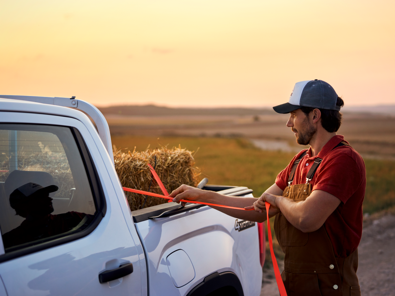 Ein Mann zurrt einen Strohballen an der Ladefläche eines Volkswagen Amarok fest.