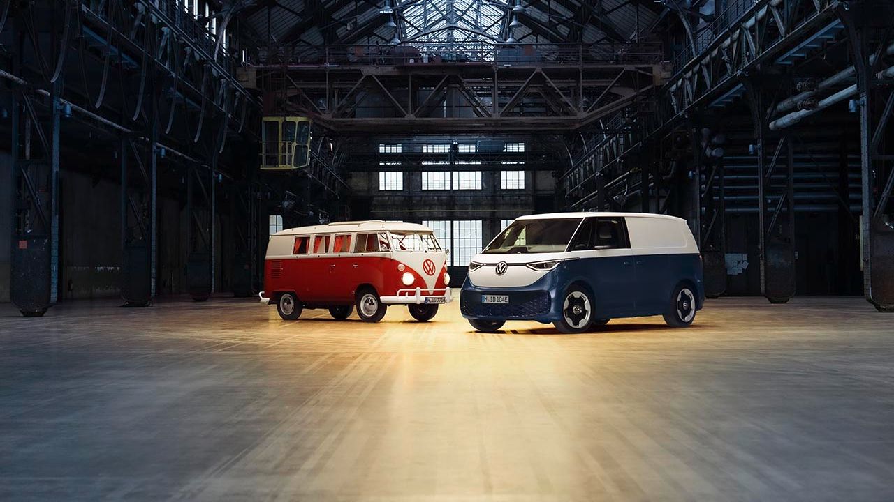 Ein roter VW Bulli und ein blauer Volkswagen ID. Buzz Cargo in schräger Seitenansicht in einer Werkshalle.