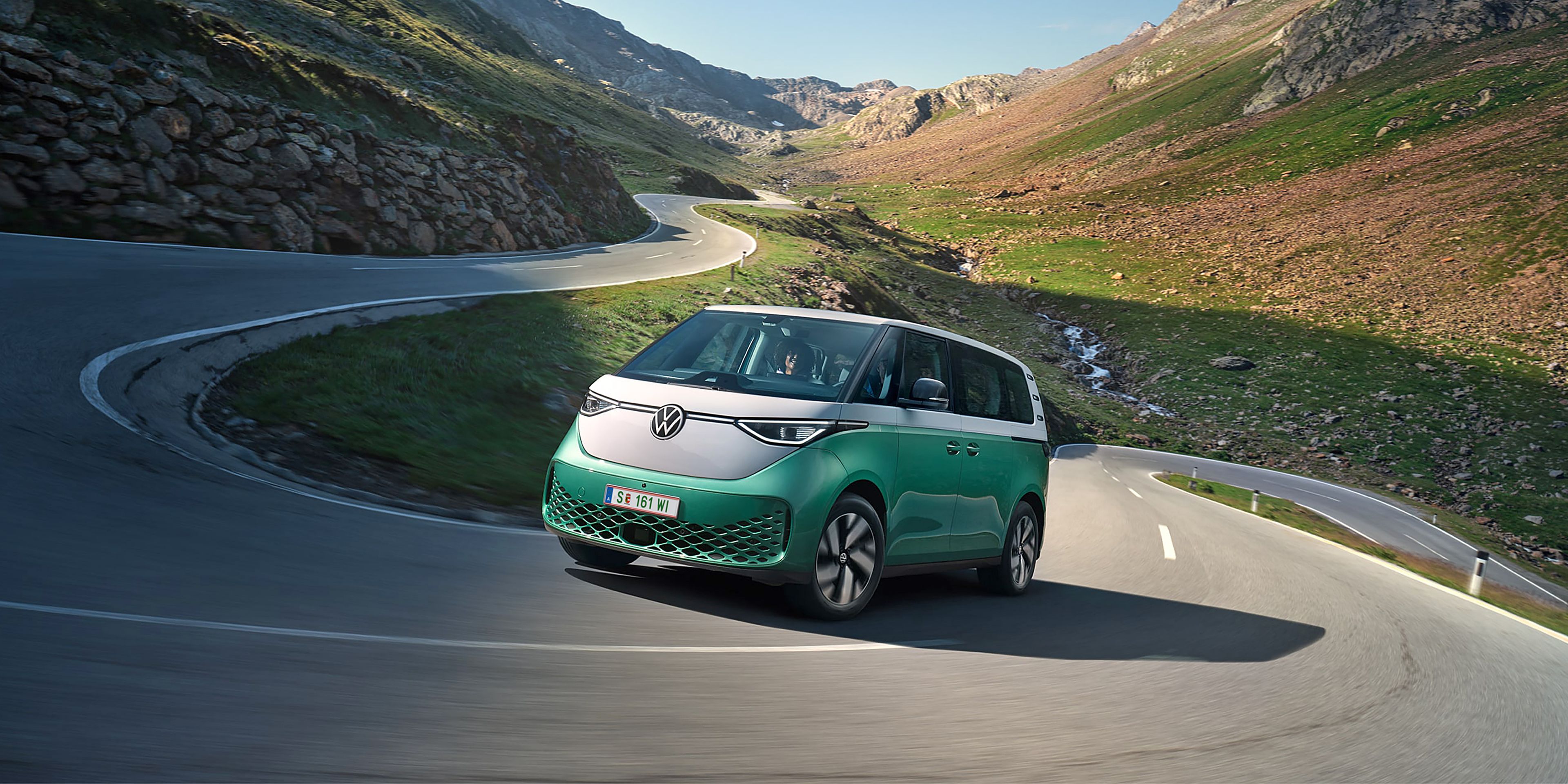 Ein grün weißer VW ID. Buzz fährt dynamisch in die Kurve einer kurvenreichen Bergstraße