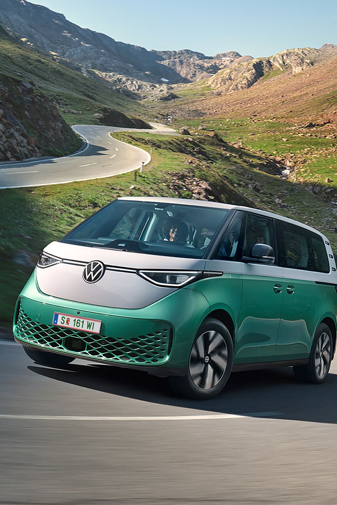 Ein grün weißer VW ID. Buzz fährt dynamisch in die Kurve einer kurvenreichen Bergstraße