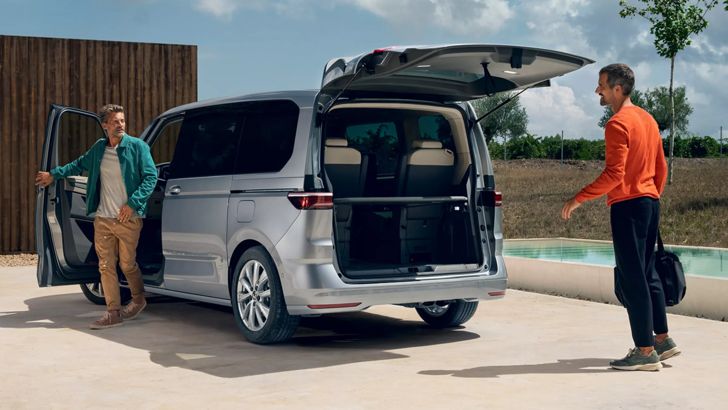 Ein Mann schließt die Fahrertür des neuen VW Multivan, ein anderer Mann wartet hinter dem Auto