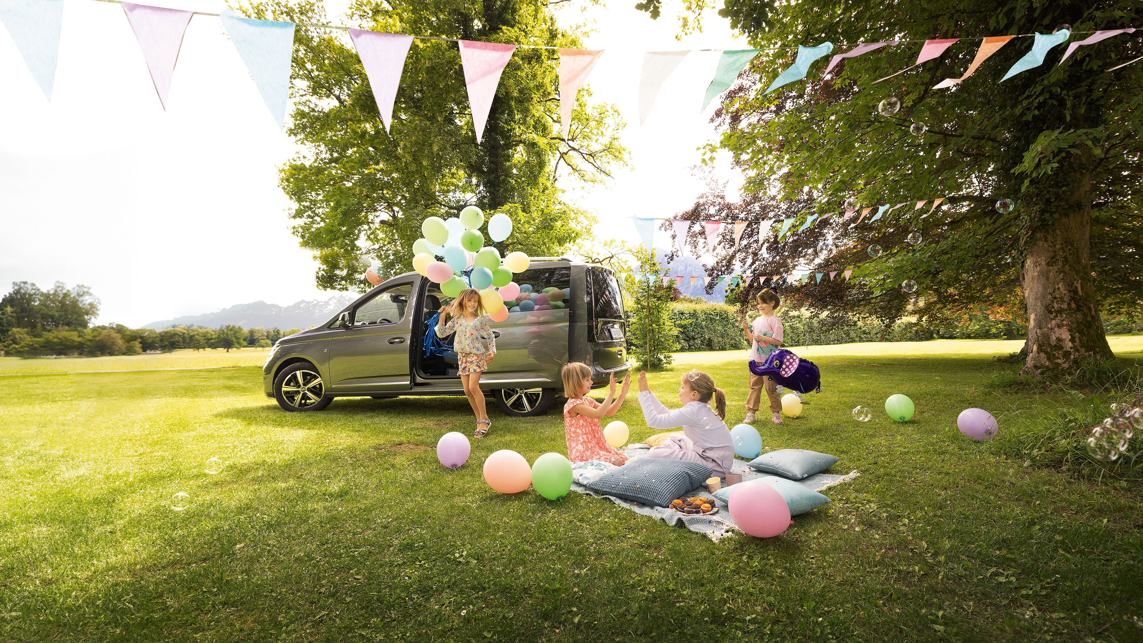 VW Caddy steht im Garten, Kinder spielen neben dem Fahrzeug und feiern Geburtstag