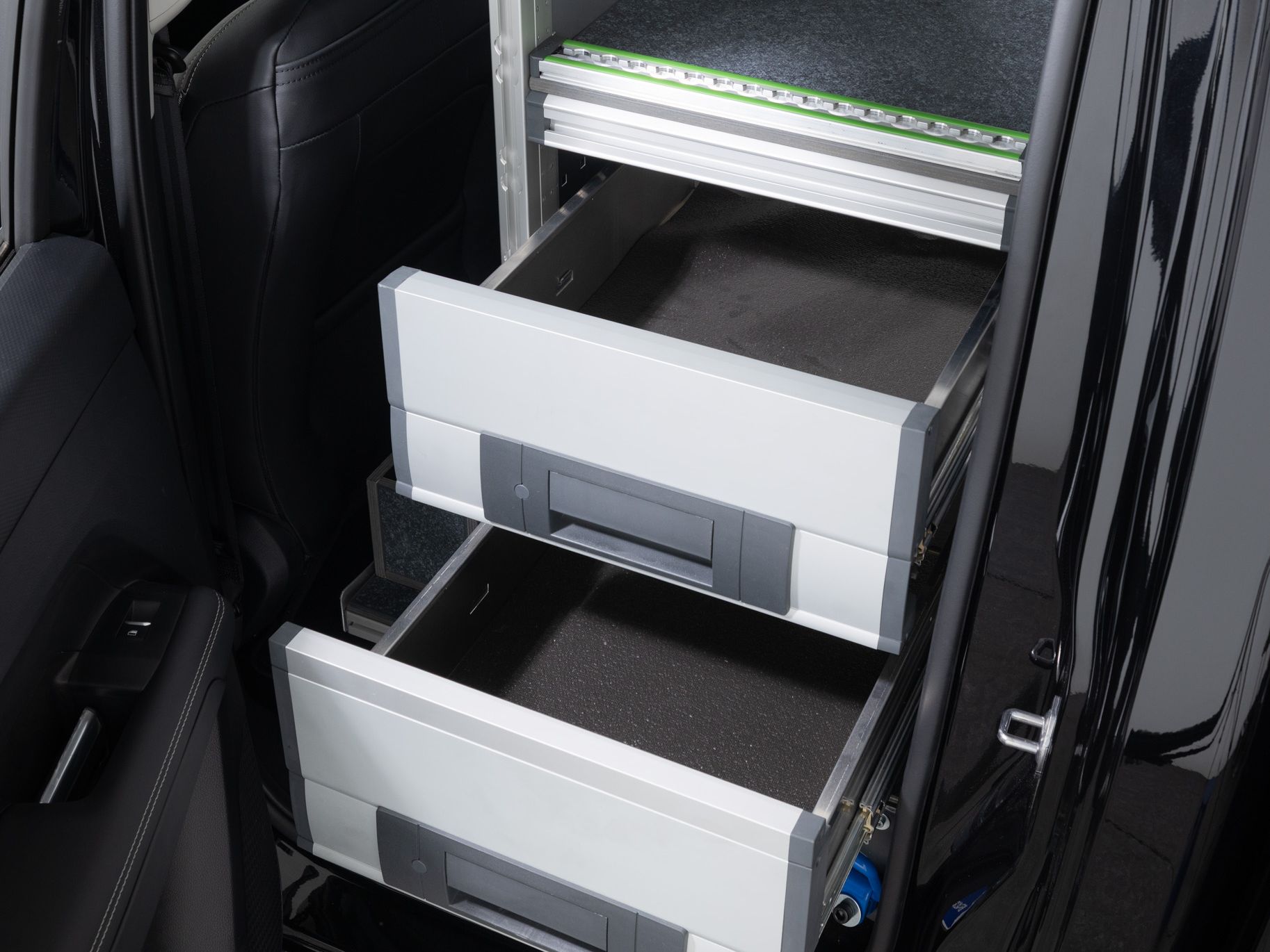 Das Bild zeigt das geöffnete Heck eines Fahrzeugs mit einem eingebauten Regalsystem. Zwei herausgezogene Schubladen sind sichtbar, jede mit einem Griff. Das Regal scheint zur Lagerung und Organisation von Werkzeugen oder anderen Materialien genutzt zu werden.