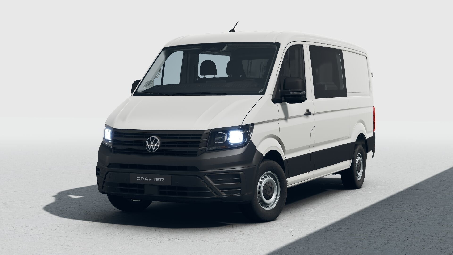Ein weißer VW Crafter Transporter steht in einem hellen Raum. Die Scheinwerfer sind eingeschaltet und der Wagen hat eine schwarze Front- und Seitentürverkleidung. Der Boden ist uneben und leicht strukturiert.