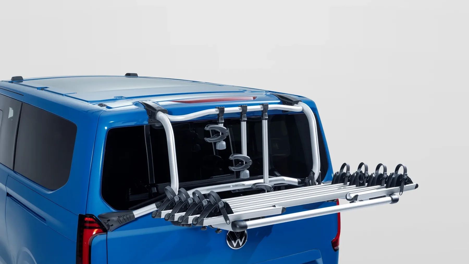 Heckansicht eines blauen Volkswagen Caravelle mit einem montierten Fahrradträger. Der silberne Träger ist aus Aluminium, nach hinten ausgeklappt und bietet mehrere Schienen für Fahrräder.