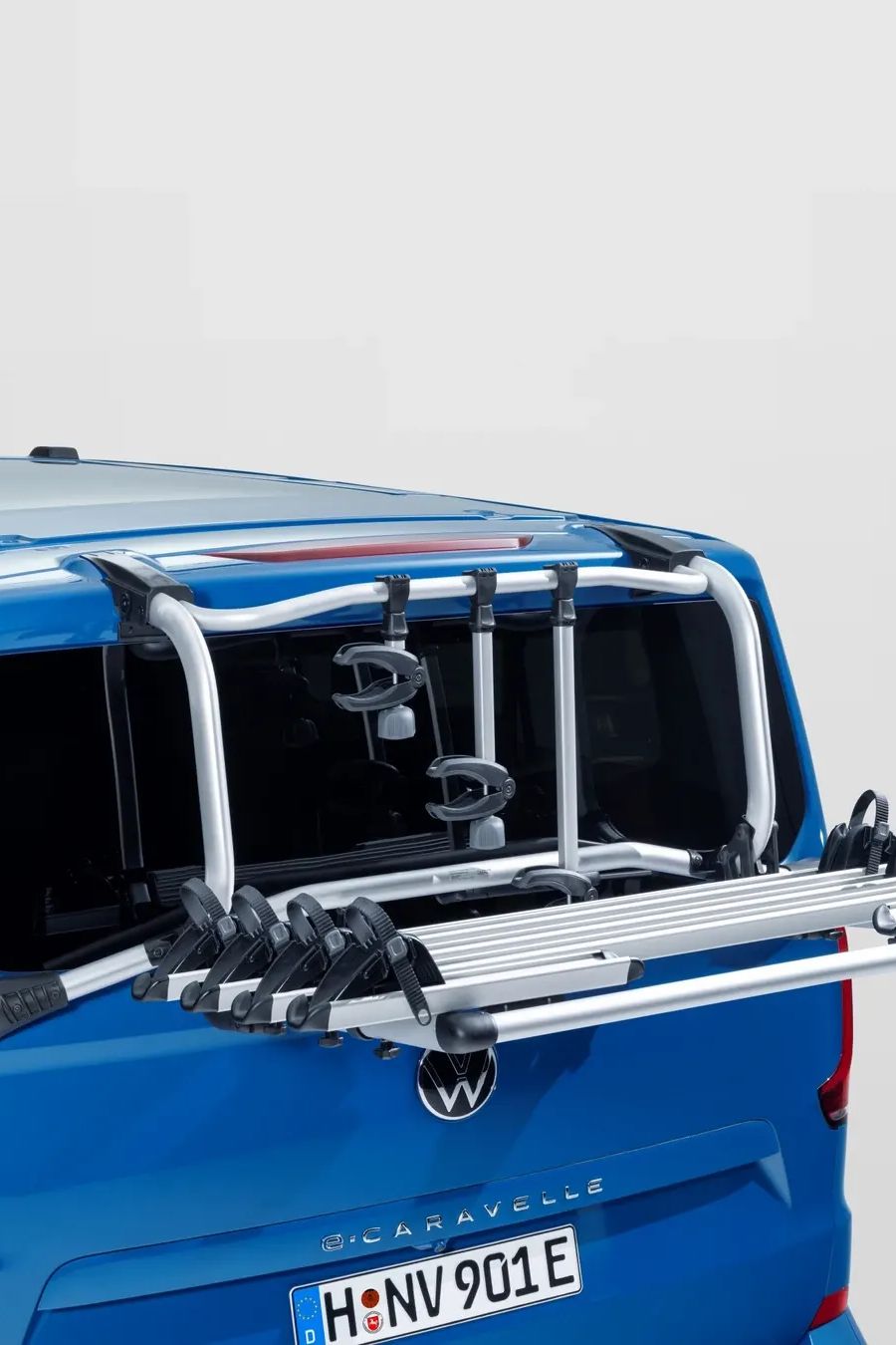 Heckansicht eines blauen Volkswagen Caravelle mit einem montierten Fahrradträger. Der silberne Träger ist aus Aluminium, nach hinten ausgeklappt und bietet mehrere Schienen für Fahrräder.