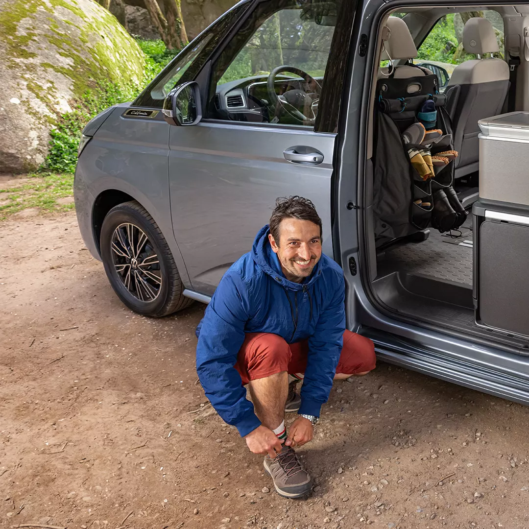 Mann zieht sich Schuhe vor VW California an.