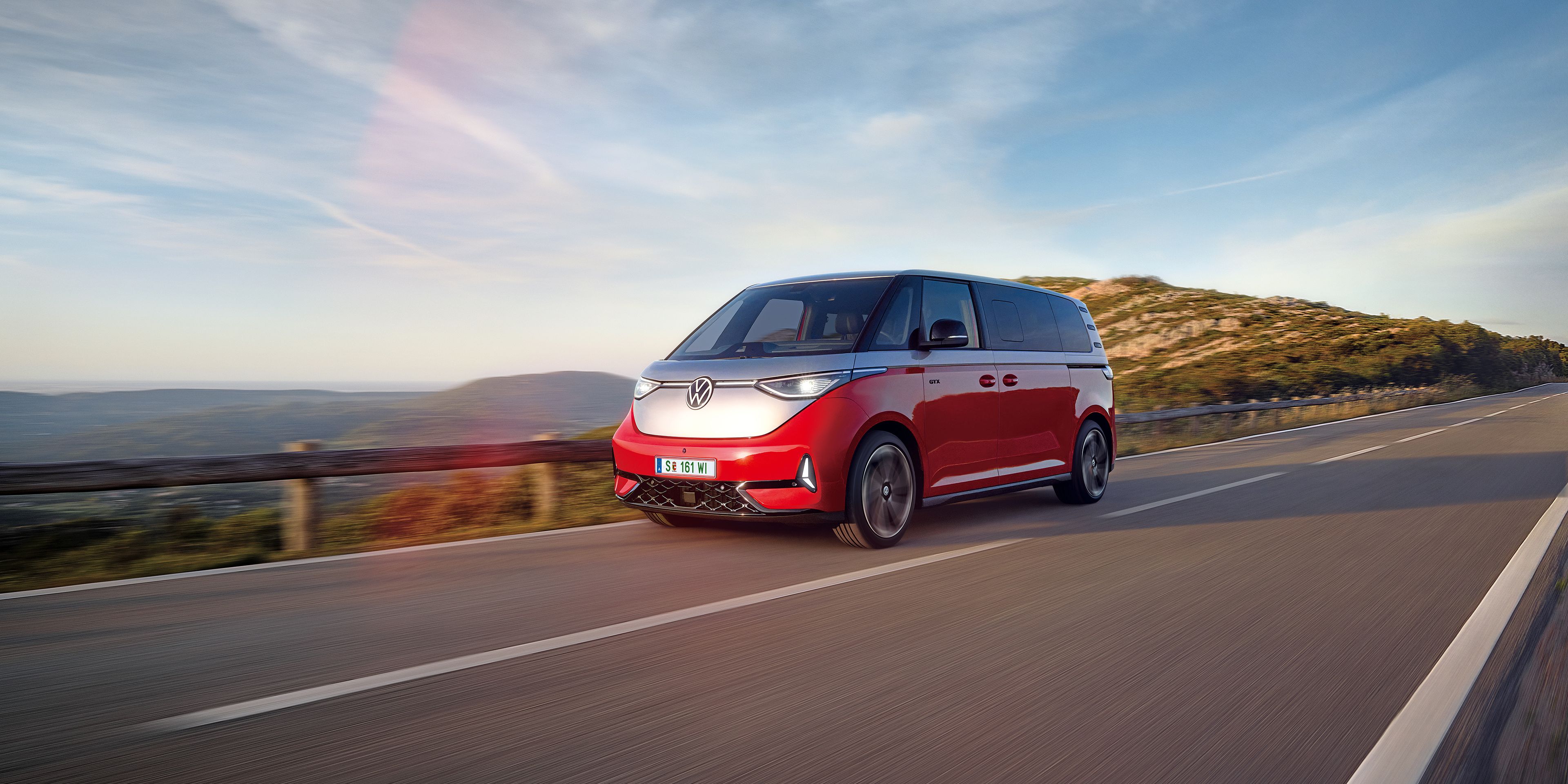 Ein rot - silberner ID. Buzz fährt entlang einer Straße in den Bergen