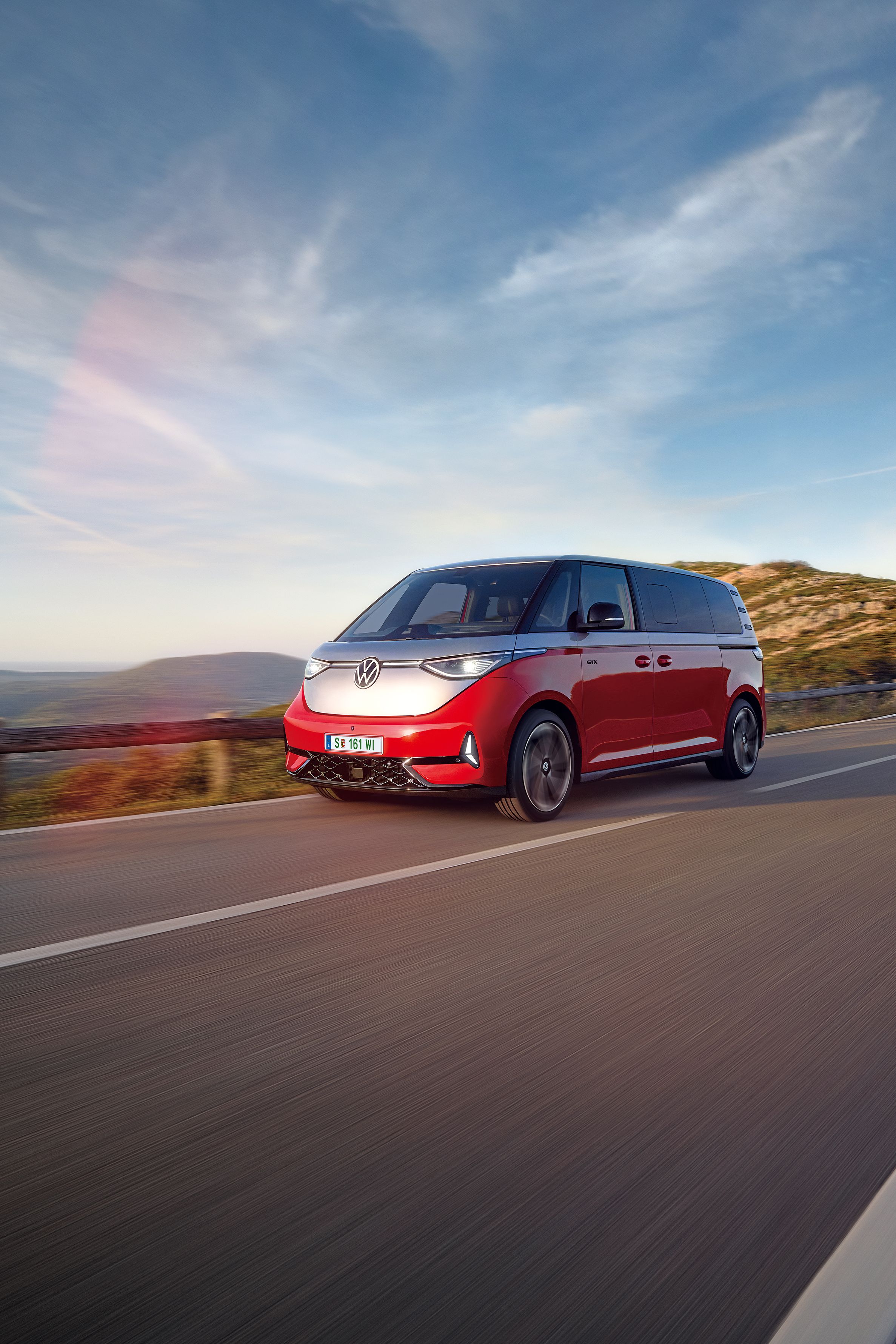 Ein rot - silberner ID. Buzz fährt entlang einer Straße in den Bergen
