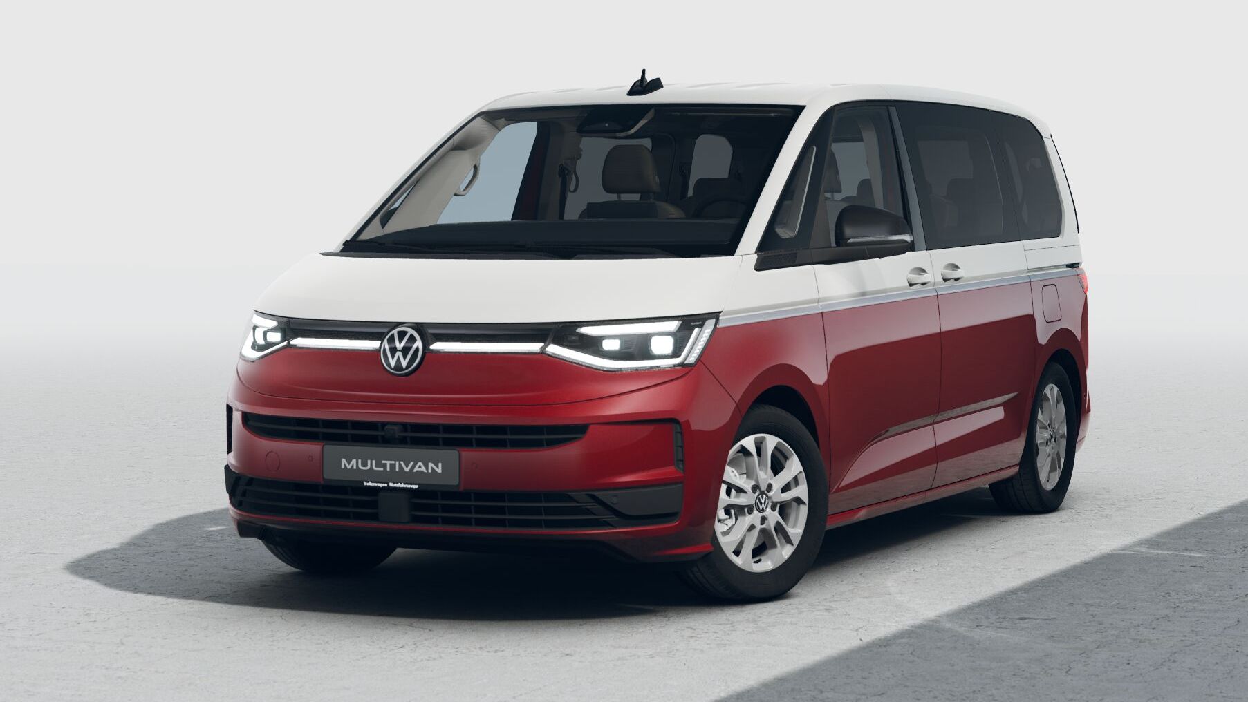 Ein rot-weißer Volkswagen Multivan steht auf einer hellen, neutralen Fläche, leicht von vorne links gesehen. Das Fahrzeug hat moderne LED-Scheinwerfer, große Fensterflächen und Schiebetüren. Die zweifarbige Lackierung betont den Familien- und Freizeitcharakter des Vans.