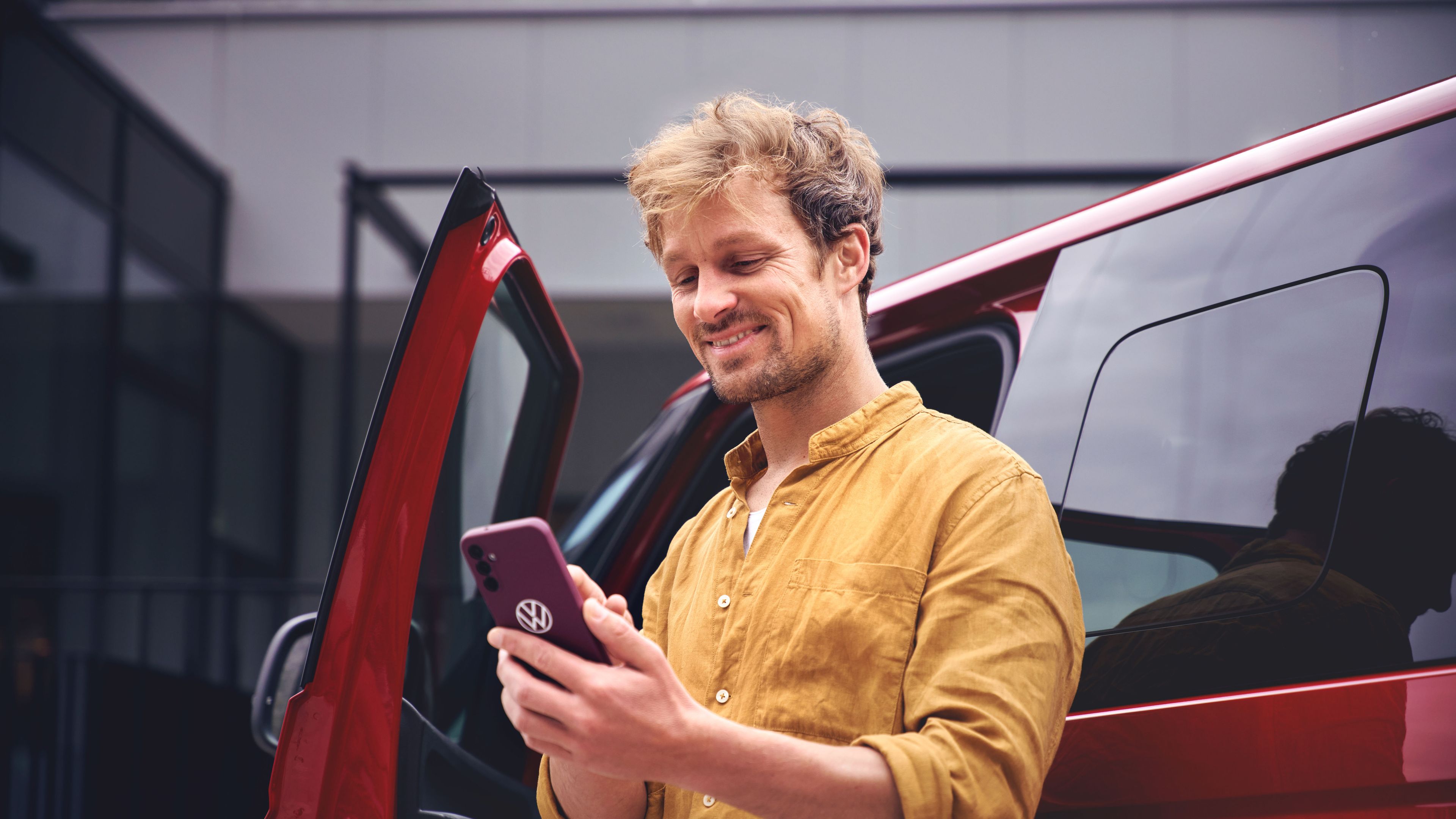 Ein Mann steht vor einem roten Volkswagen Nutzfahrzeug und tippt in sein Smartphone.