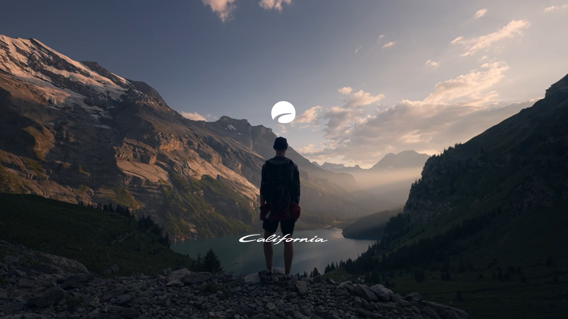 Eine Person steht auf einem felsigen Abhang und schaut auf eine Berglandschaft mit einem See im Tal. Der Schriftzug "California" ist in der Mitte des Bildes platziert.